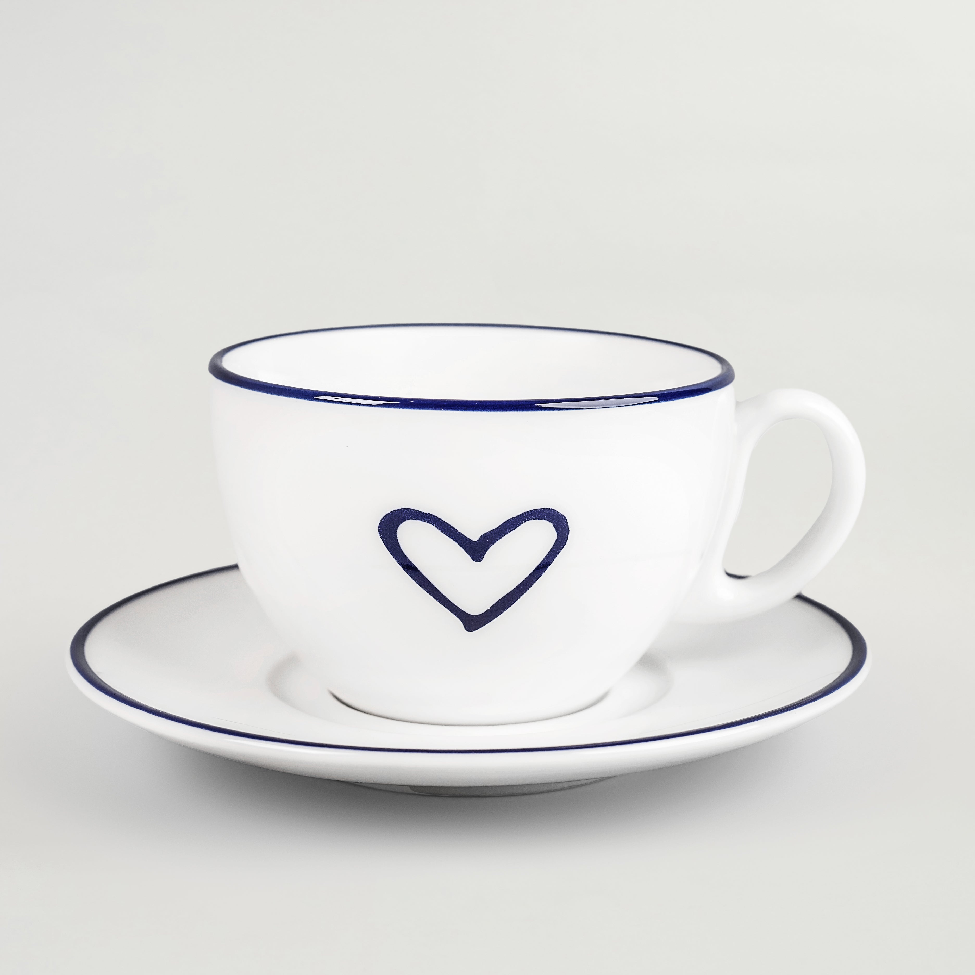 A white porcelain cappuccino and tea set with a blue heart design on the cup, consisting of one plate and one cup.