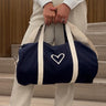 A person standing on stairs holding a navy and white duffle bag with a heart shape on the side.