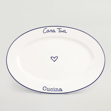 A white ceramic serving platter with blue rim and text that reads 'Casa Tua' on the top and 'Cucina' on the bottom, with a heart symbol between the two words.