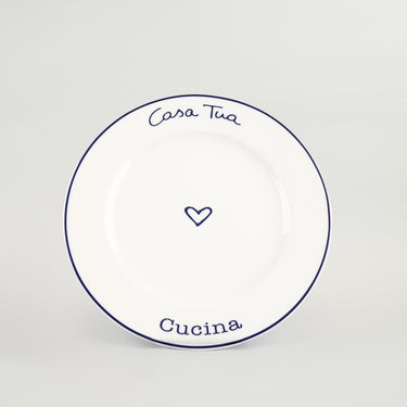 A white ceramic plate with blue rim and text reading 'Casa Tua Cucina' along with a heart symbol in the center.