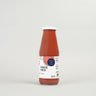 A bottle of tomato puree with a white cap and a label that includes the text 'Tomato Puree' and 'Passata'. The background is plain and the bottle is upright.