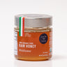 A jar of honey labeled '100% Organic Pure Raw Honey' with a red and white brand tag indicating it's a product of Italy.